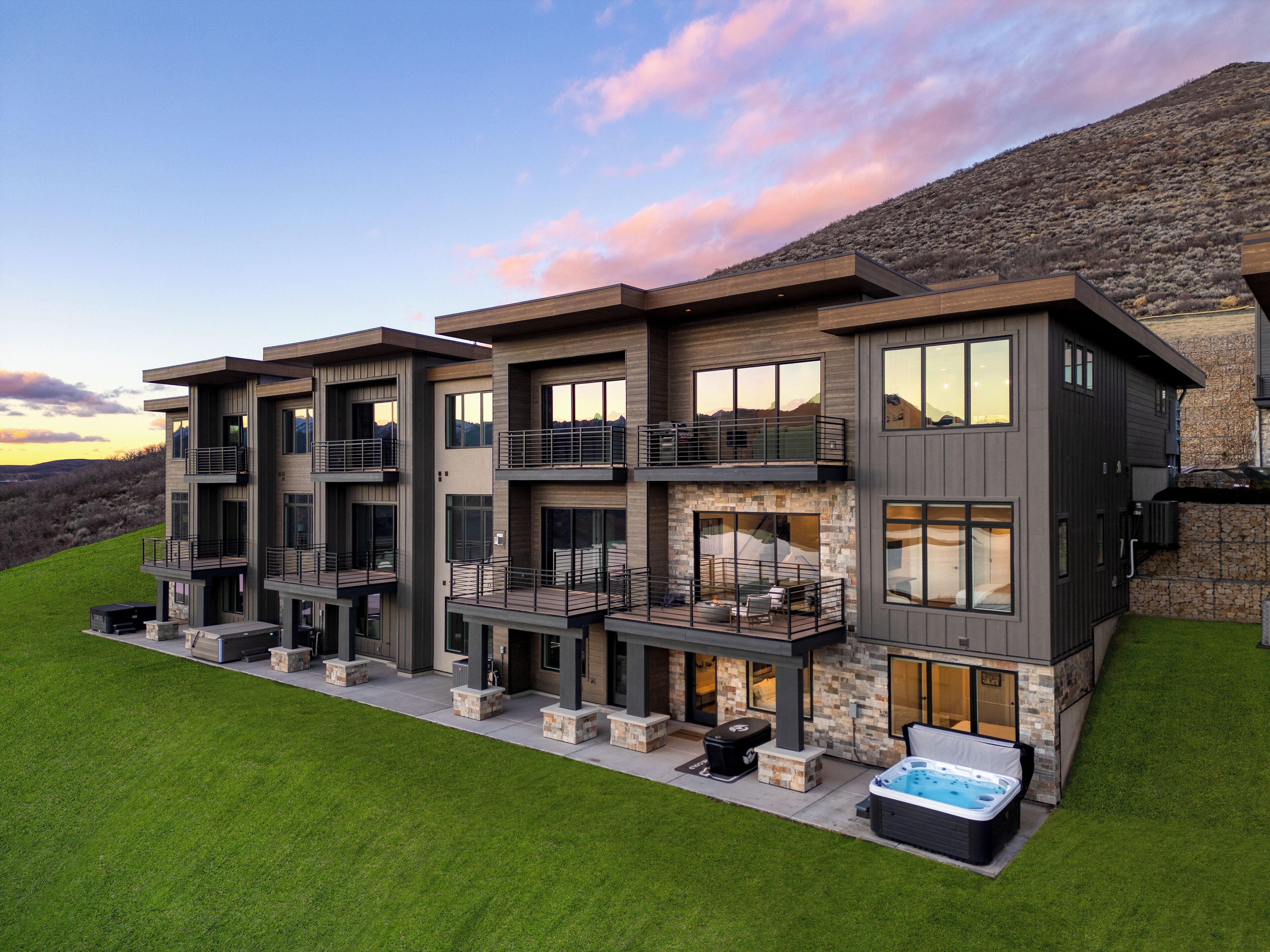 A multi-story modern house with balconies, a hot tub, and a stone facade.