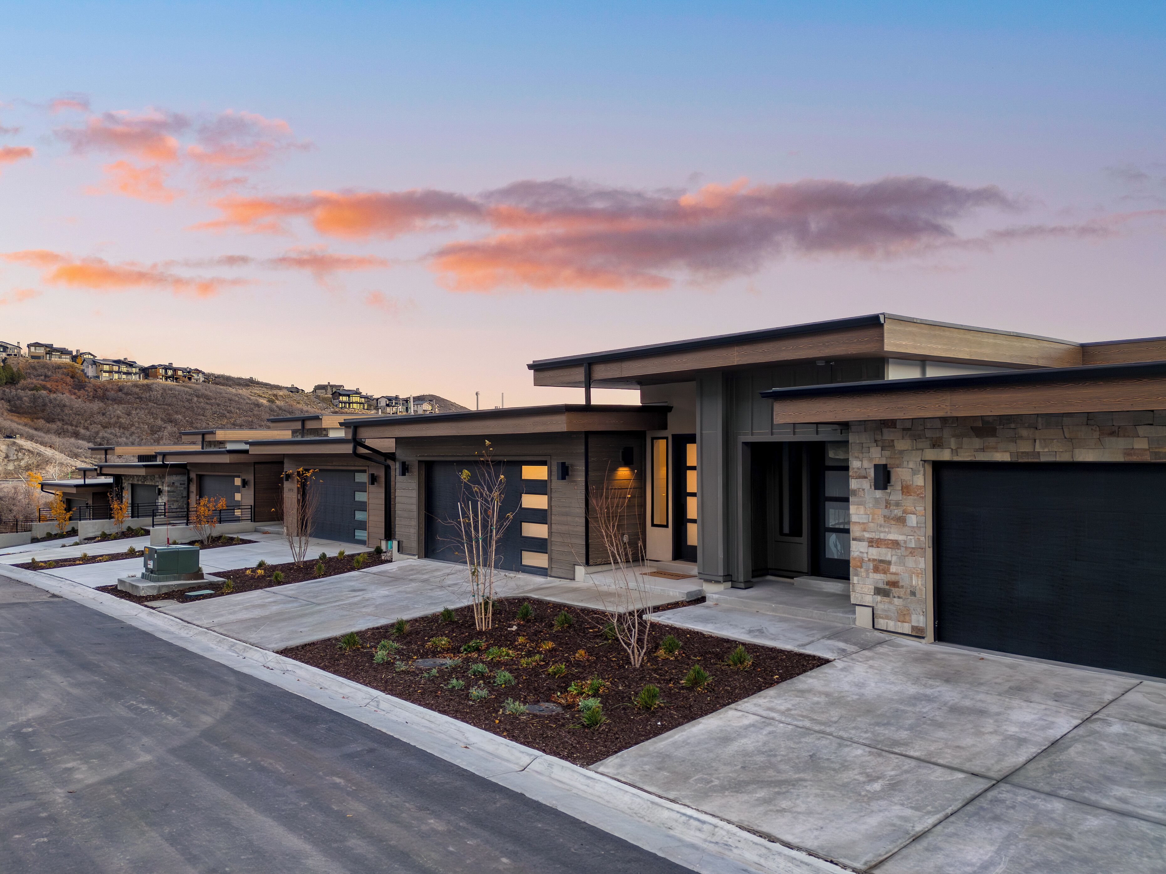 Un immeuble résidentiel moderne doté de plusieurs garages, d’un jardin paysager à l’avant et d’un paysage vallonné en arrière-plan.