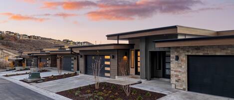 Un immeuble résidentiel moderne doté de plusieurs garages, d’un jardin paysager à l’avant et d’un paysage vallonné en arrière-plan.