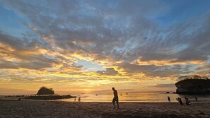 Eine Strandansicht mit Menschen, einem Sonnenuntergang und einer Felsformation.