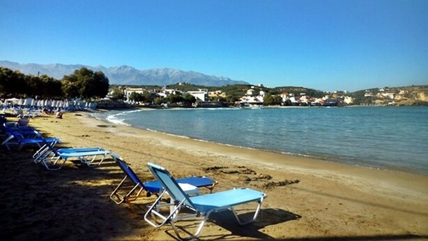 Ein Strand mit Liegen und Blick auf das Meer und ferne Berge.