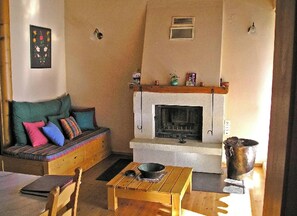 A cozy living room with a fireplace, a sofa with colorful cushions, and a wooden table with a bowl. - Kamares – a restaured Venetian domain retreat (Macheri)