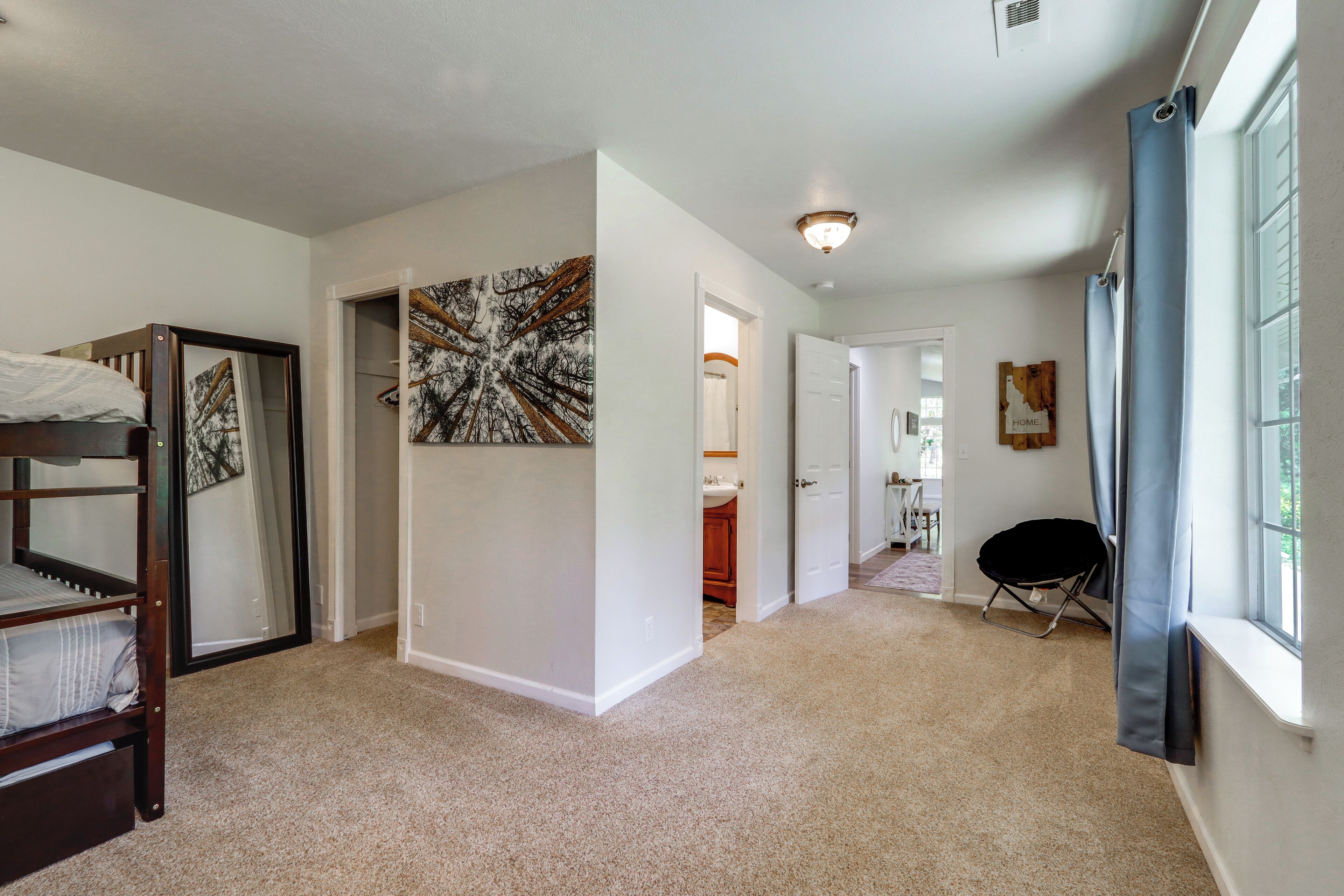 A bedroom with a bunk bed, a hallway leading to a bathroom, and a large window with curtains.
