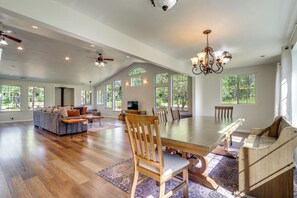 A spacious living area with a large dining table, multiple chairs, a sofa, and a television. - Riffle Road Ranch: 10 Acres, 8 Mi to Silverwood (Spirit Lake)