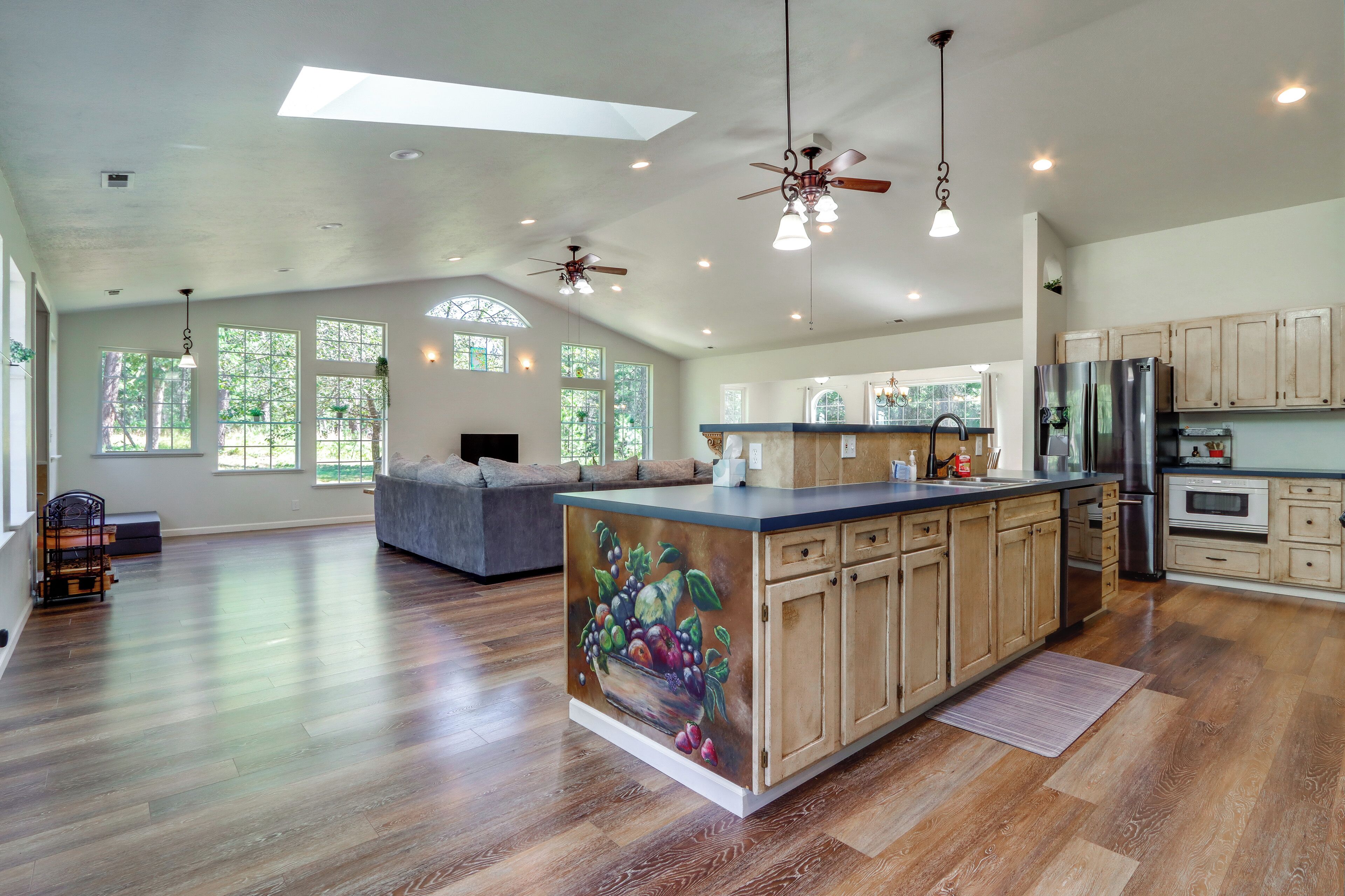 A spacious kitchen with a central island, wooden cabinets, and a large window.
