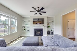 A living room with a fireplace, a ceiling fan, and a large window. - Fenced Yard! Monthly Stay, 4 Mi to Dtwn Clayton (Clayton)