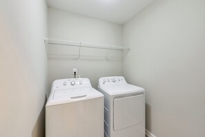 Une buanderie avec deux machines à laver et deux sèche-linge blancs, un étendoir métallique et un mur blanc.