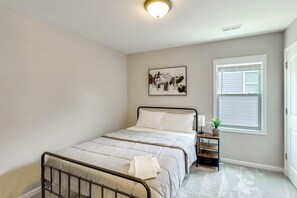 A bedroom with a bed, a bedside table, a window with blinds, a ceiling light, and a wall-mounted artwork. - Fenced Yard! Monthly Stay, 4 Mi to Dtwn Clayton (Clayton)