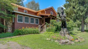 A two-story house with a stone foundation, a wooden deck, and a stone staircase leading to the entrance. - On Horse Farm! Home w/ Pond Access in Spring Creek (Spring Creek)