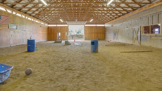 An indoor arena with a wooden ceiling, sandy floor, and a large open space. - On Horse Farm! Home w/ Pond Access in Spring Creek (Spring Creek)