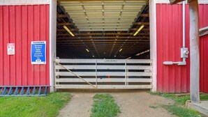 A red barn entrance with a warning sign, a gate, and a dirt path leading inside. - On Horse Farm! Home w/ Pond Access in Spring Creek (Spring Creek)