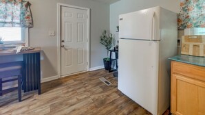 A kitchen with a white refrigerator, wooden flooring, a door, and a window with floral curtains. - 1 Mi to Fort Valley State College! Home w/ Grill (Fort Valley)