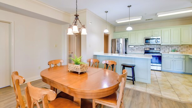A modern kitchen with light green cabinets, stainless steel appliances, and a wooden dining table with chairs. - Pool Access + Golf View: 5BR Springfield Home (Springfield)