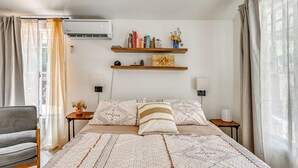 Ein Schlafzimmer mit einem Bett, zwei Nachttischen, einem Sessel und einem Wandregal mit Büchern und Dekoration.