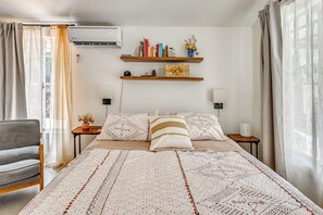 Ein Schlafzimmer mit einem Bett, zwei Nachttischen, einem Sessel und einem Wandregal mit Büchern und Dekoration.