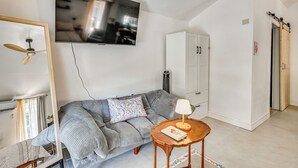 Ein Wohnzimmer mit einer Couch, einem an der Wand montierten Fernseher, einem Deckenventilator, einem Schrank und einem kleinen Tisch mit einer Lampe.