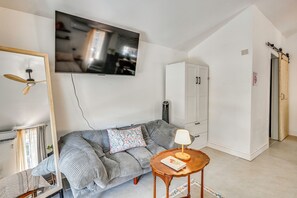 Ein Wohnzimmer mit einer Couch, einem an der Wand montierten Fernseher, einem Deckenventilator, einem Schrank und einem kleinen Tisch mit einer Lampe.