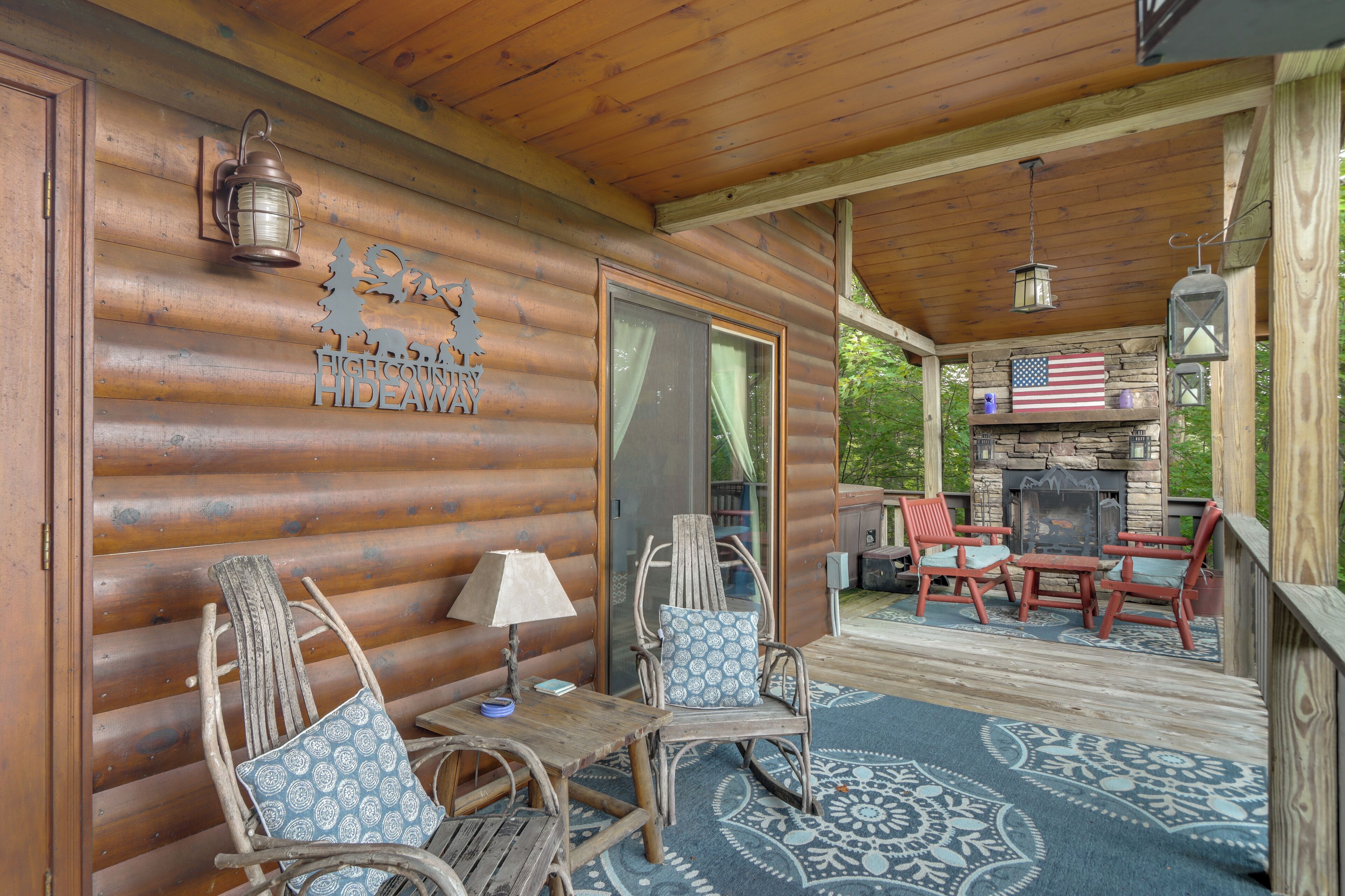 A wooden cabin with a covered porch, a stone fireplace, and outdoor seating.