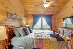 Ein Schlafzimmer einer Holzhütte mit einem Bett, einem Fernseher und einem Fenster mit Vorhängen.