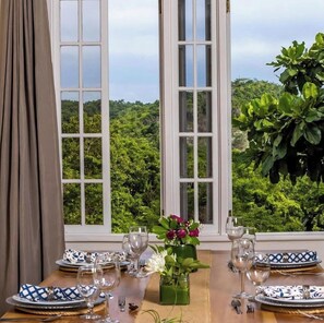 A dining table with glasses and a vase of flowers, set against a backdrop of a window with a view of a lush green landscape. - Pvt Villa Estate with Mtn Views  Pool in Ocho Rios (Labyrinth)
