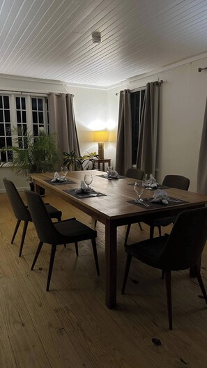 Een eetruimte met een lange houten tafel, zes stoelen, een lamp en een raam met gordijnen.