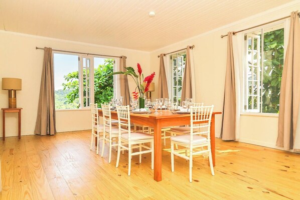 Ein Esszimmer mit einem Holztisch, gedeckt für sechs Personen, weißen Stühlen und einer Vase mit roten Blumen.