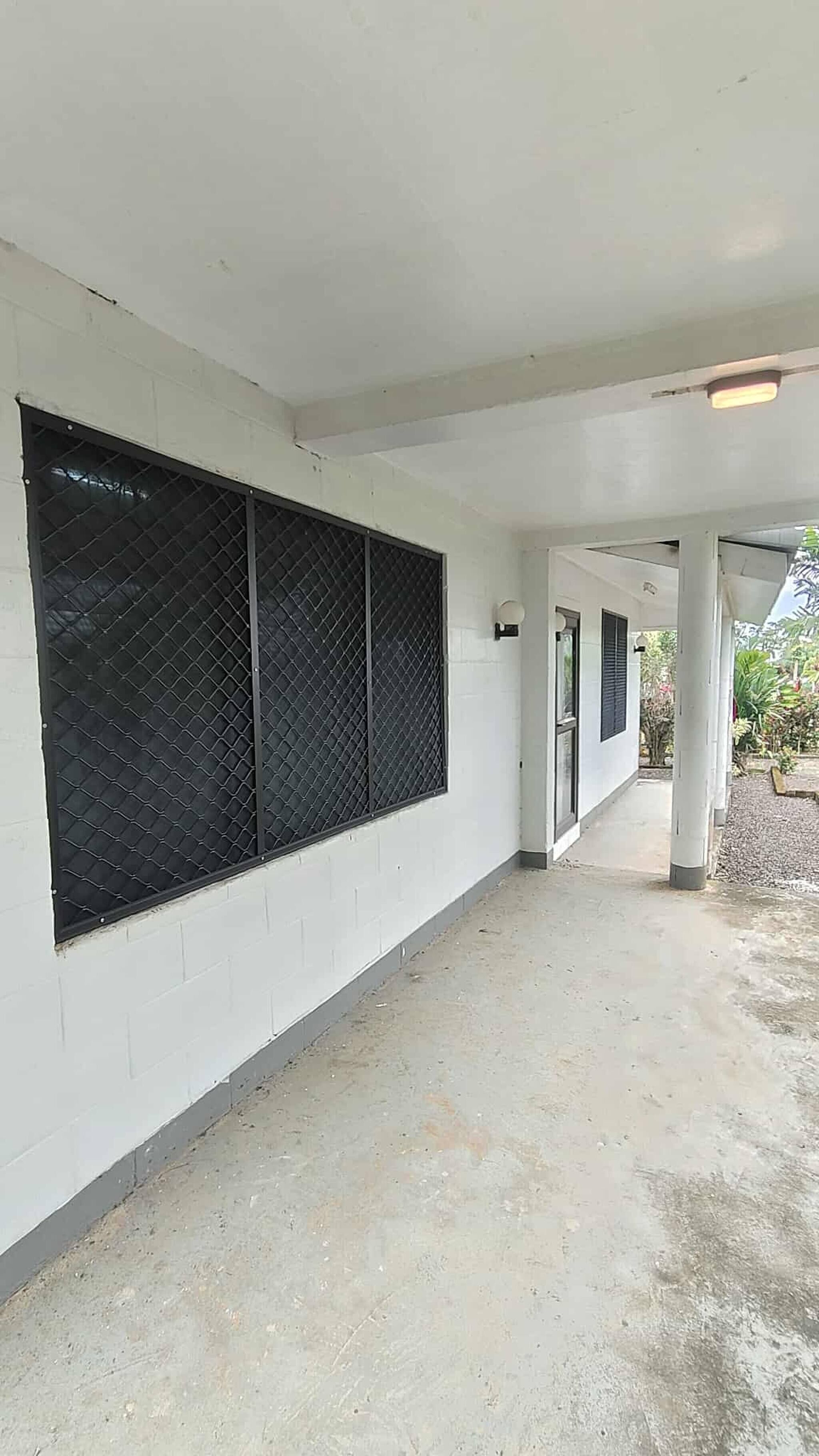 Un pasillo cubierto con pared blanca, cerca metálica y suelo de hormigón.
