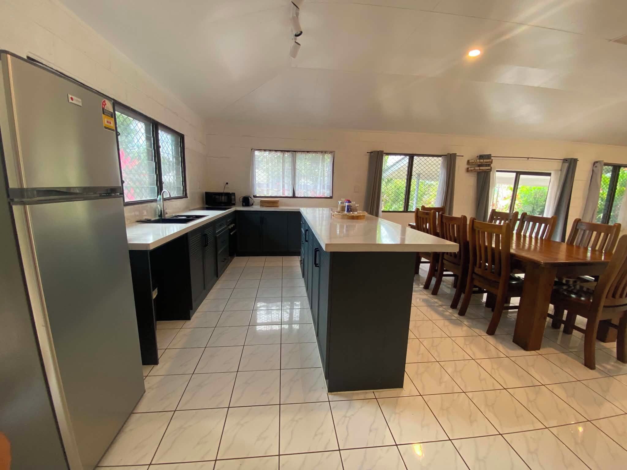 Una cocina amplia con una isla central, muebles oscuros y una zona de comedor con sillas de madera.