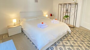 Ein Schlafzimmer mit einem Bett, Nachttischen, einer Pendelleuchte, einer Zimmerpflanze und einem gestreiften Boden.