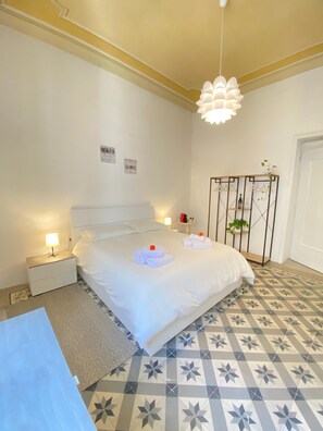 A bedroom with a bed, bedside tables, a hanging light fixture, a decorative plant, and a patterned floor. - Sea & Sun Suite (Cagliari)
