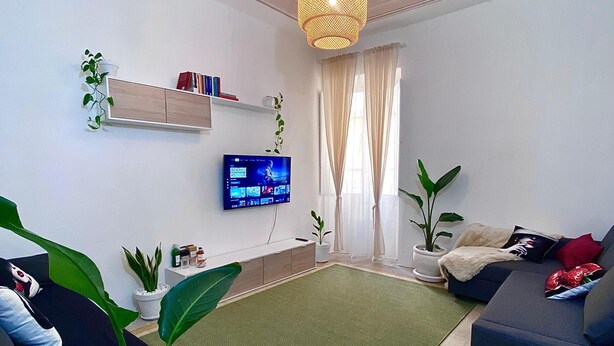 Ein modernes Wohnzimmer mit Flachbildfernseher, einer Couch, einem Couchtisch und einer dekorativen Deckenleuchte.