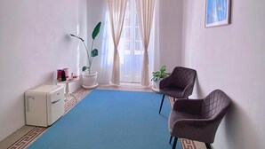 Ein Zimmer mit blauem Teppich, einem weißen Heizkörper, einer Topfpflanze, einem gerahmten Bild an der Wand und einem Sessel.