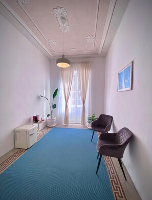 A room with a blue carpet, a white radiator, a potted plant, a framed picture on the wall, and a chair. - Sea & Sun Suite (Cagliari)