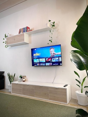 A flat-screen TV mounted on a wall, a wooden cabinet below, and a potted plant to the right. - Sea & Sun Suite (Cagliari)