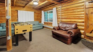 Una habitación acogedora con paredes de madera, un sofá de cuero, una mesa de fútbol y una ventana con cortinas.