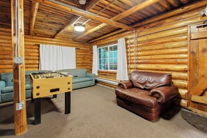 A cozy room with wooden walls, a leather sofa, a foosball table, and a window with curtains.