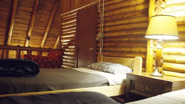 Un dormitorio de cabaña de madera con dos camas, un cabecero de madera, una lámpara de noche y una puerta.