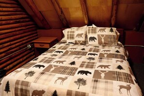 A log cabin bedroom with a plaid-patterned bedspread featuring animal prints, a wooden nightstand, and a simple bedside table.