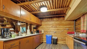 Cocina de cabaña de troncos con armarios de madera, cafetera, microondas y un lavabo.