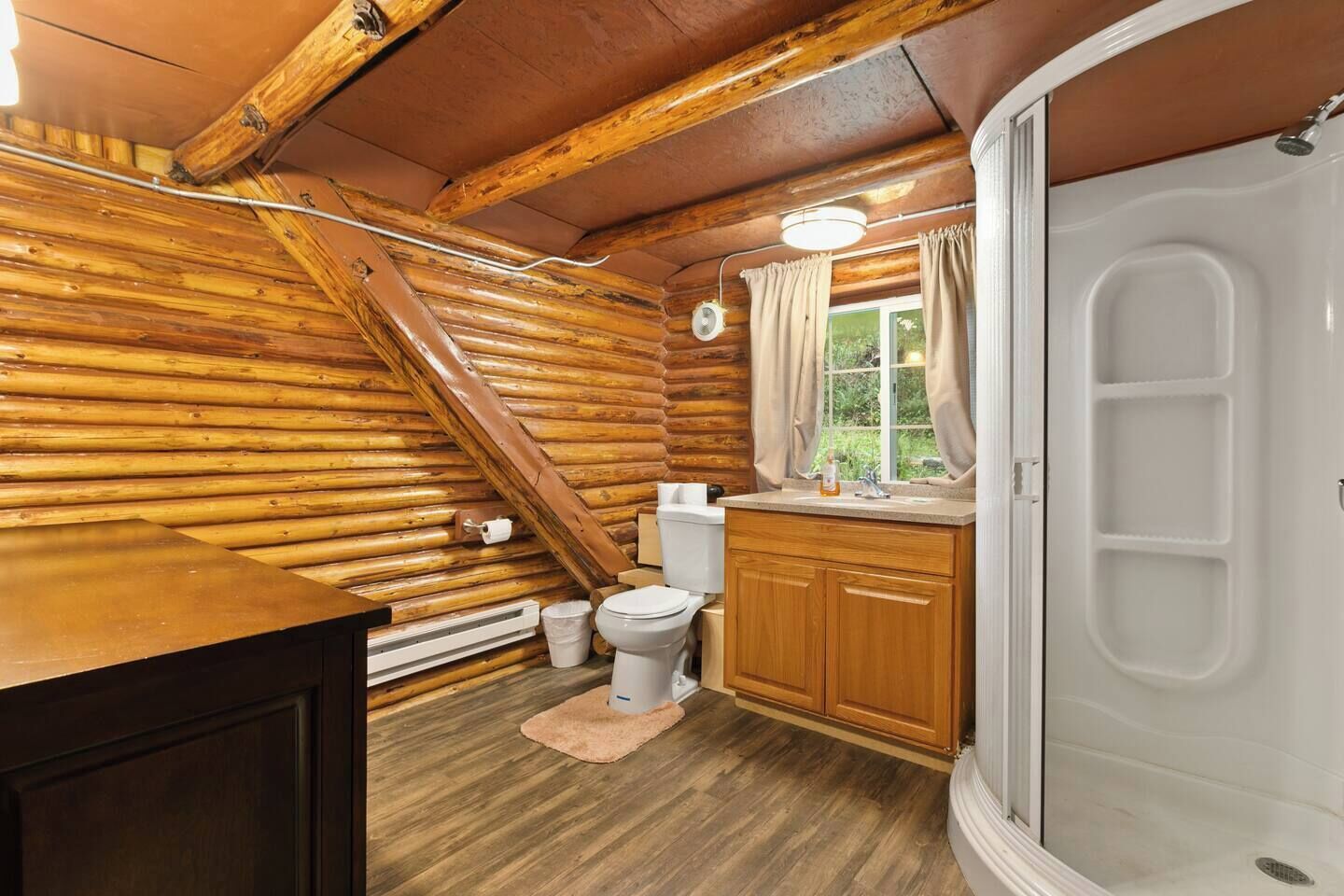 A log cabin bathroom with a toilet, sink, and shower.