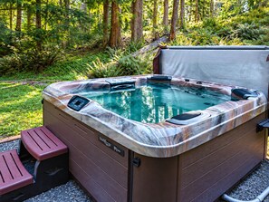 Een hottub met bedieningspaneel, omgeven door een houten terras en een bosrijke achtergrond.