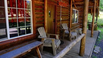 Une cabane en rondins avec une véranda, des chaises en bois et un banc.