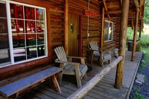 A log cabin with a porch, wooden chairs, and a bench.