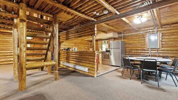A log cabin interior with a dining area, kitchen, and a wooden ladder.