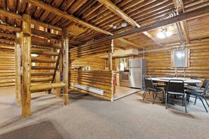 A log cabin interior with a dining area, kitchen, and a wooden ladder.