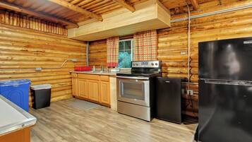 A log cabin kitchen with wooden walls, a stove, a refrigerator, and a sink.