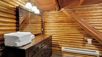 A wooden cabin bathroom with a wooden sloped ceiling, a vanity with a mirror, a towel stack, and a towel dispenser.