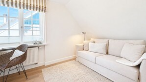 En moderne stue med en hvid sofa, en fletstol, en radiator og et vindue med gardin i striber.