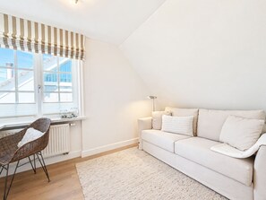Ein modernes Wohnzimmer mit einem weißen Sofa, einem Korbstuhl, einer Heizung und einem Fenster mit einem gestreiften Vorhang.