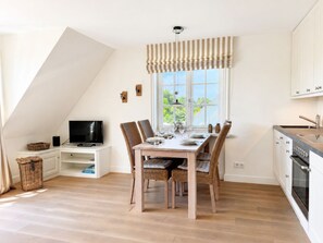 A dining area with a table set for four, a television on a stand, and a kitchen with a stove and cabinets. - Sünnsiet - Süünsiet: Modern vacation rental with a sunny south-facing balcony in (Wenningstedt-Braderup (Sylt))